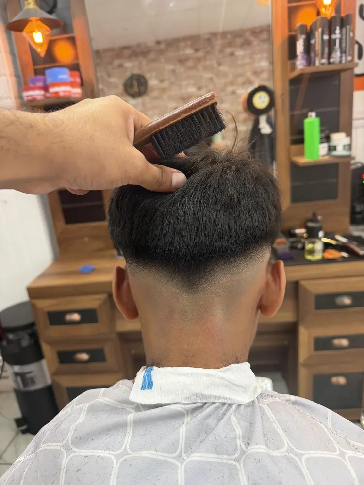 Barber brushing a client's hair after a fade at the mirror station